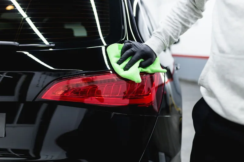 A person is cleaning the tail light of a car with a green cloth.