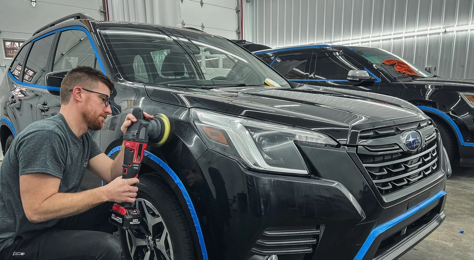 A man is polishing a black suv in a garage.