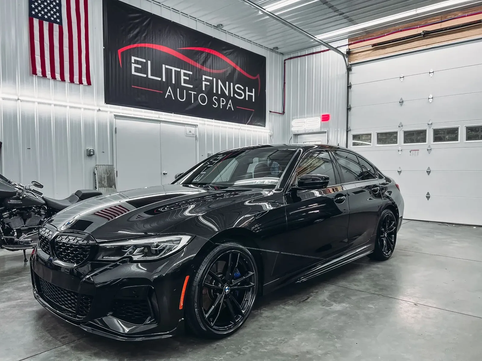 A black car is parked in a garage next to an american flag.