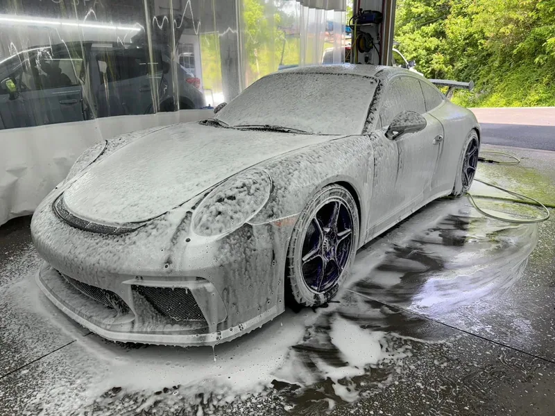 A porsche 911 is covered in foam at a car wash.
