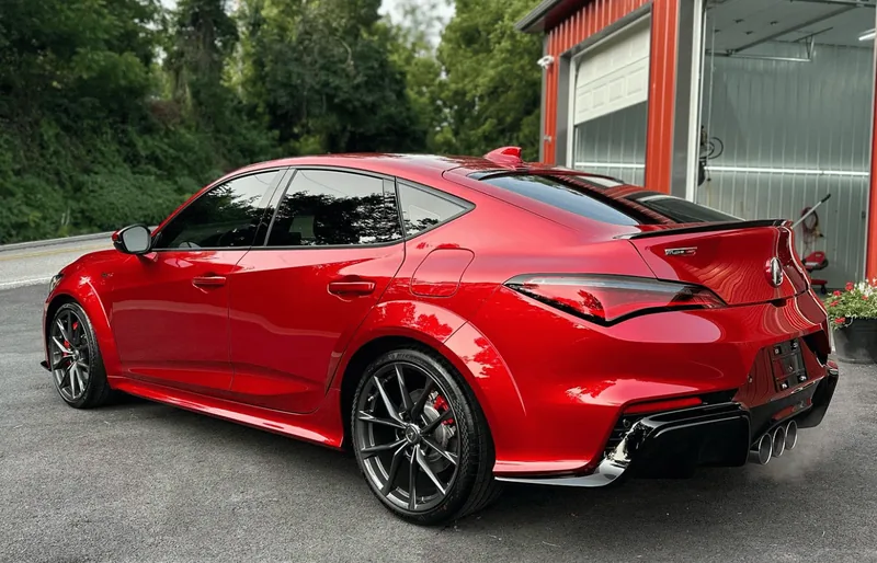 Red sports coupe parked outside a garage, shown from the rear three-quarter angle.
